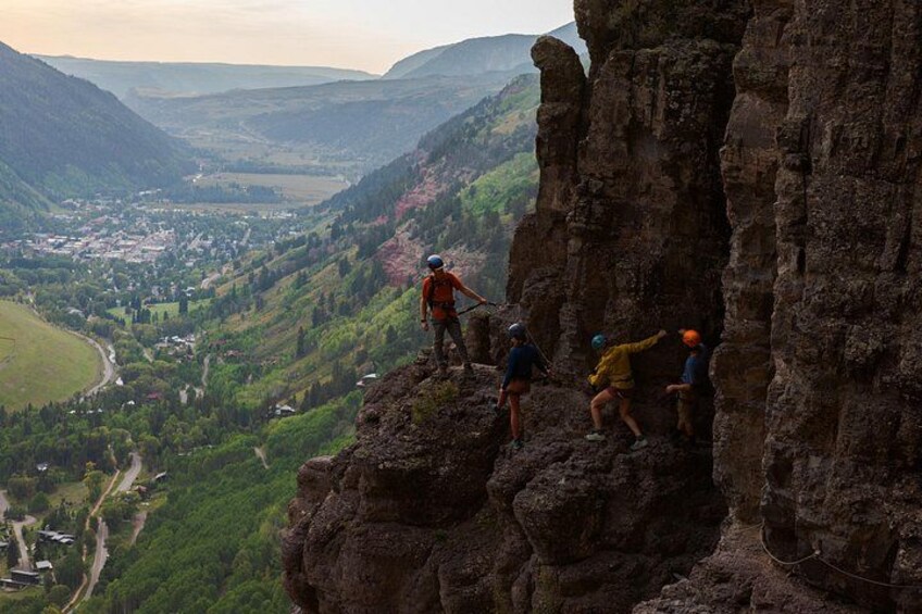 A group of climbers on a rocky cliff with a valley below. 2