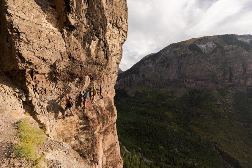 A group of climbers ascending a steep rock face with a mountainous landscape in the background. 3