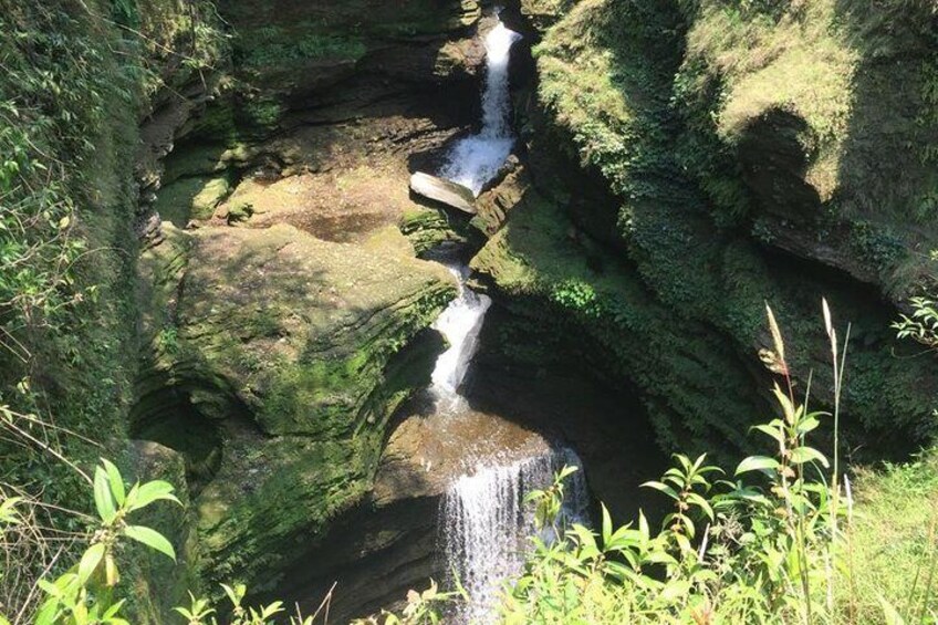 A waterfall cascading down moss-covered rocks in a forested area. 2