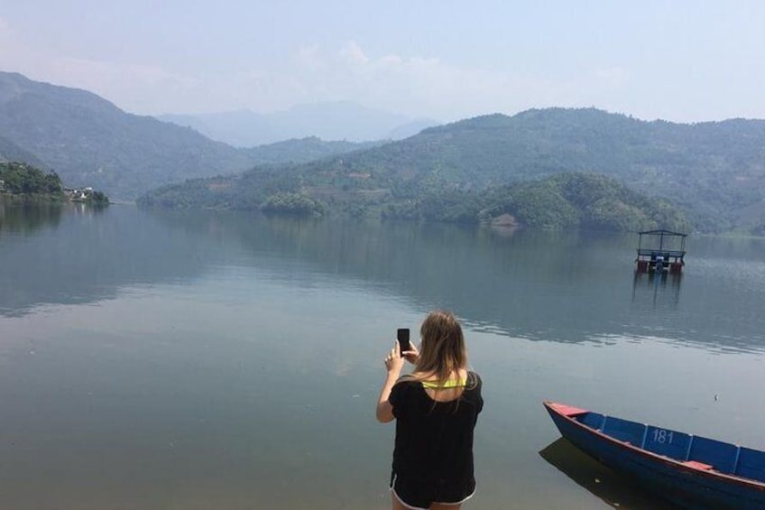 A person taking a photo of a lake with boats and hills in the background. 5