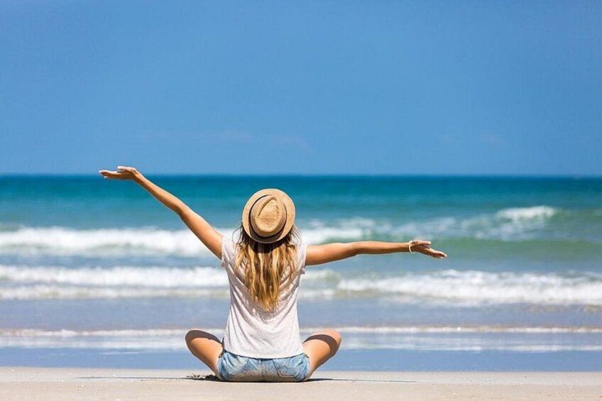 A person sitting on the beach facing the ocean with arms outstretched. 2