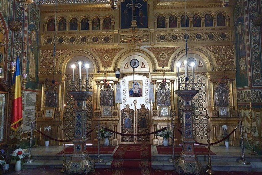 Een rijk versierd kerkinterieur met religieuze iconen, een rode loper en een vlag. 4