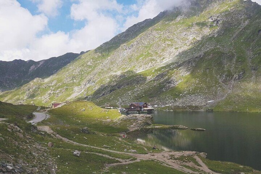 Un paisaje montañoso con un lago, una construcción pequeña y un sendero. 4