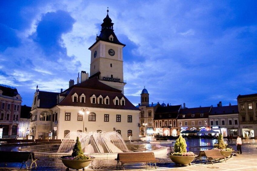 Un edificio storico con una torre dell'orologio, una fontana e una piazza ben illuminata al crepuscolo. 3