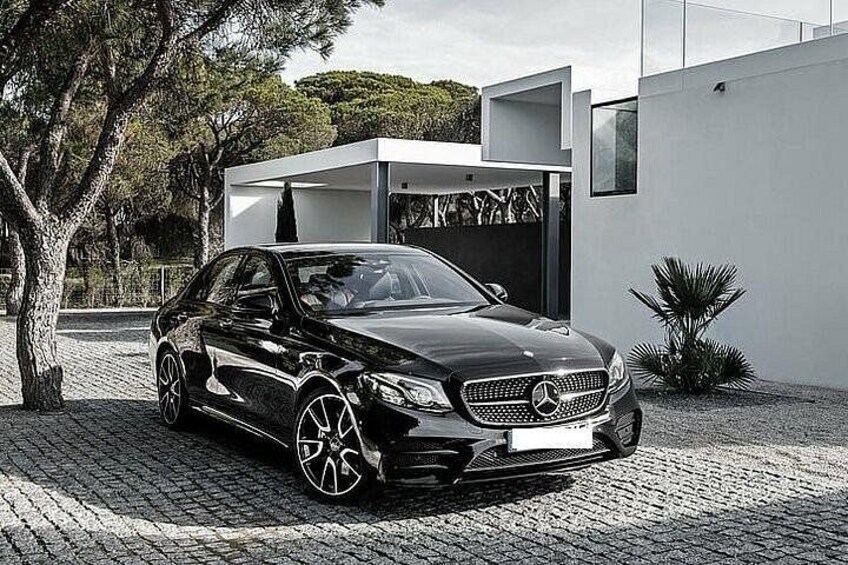 A black Mercedes-Benz parked in front of a modern house with a garage. 2