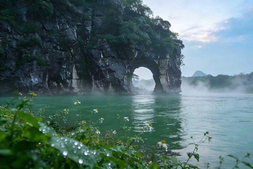 A natural rock arch over a body of water with greenery in the foreground. 1