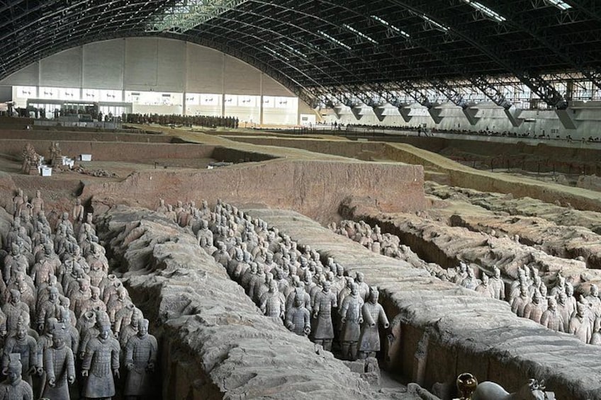 Terracotta soldiers arranged in rows, a large open space with a high ceiling, and a building in the background. 2