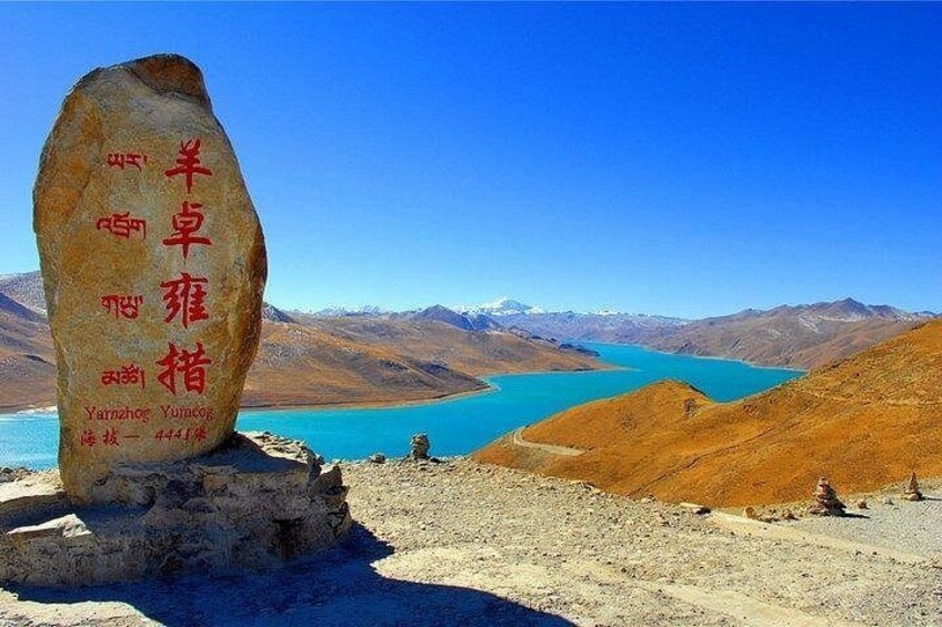 A large rock with inscriptions, a clear blue sky, and a lake surrounded by mountains. 5