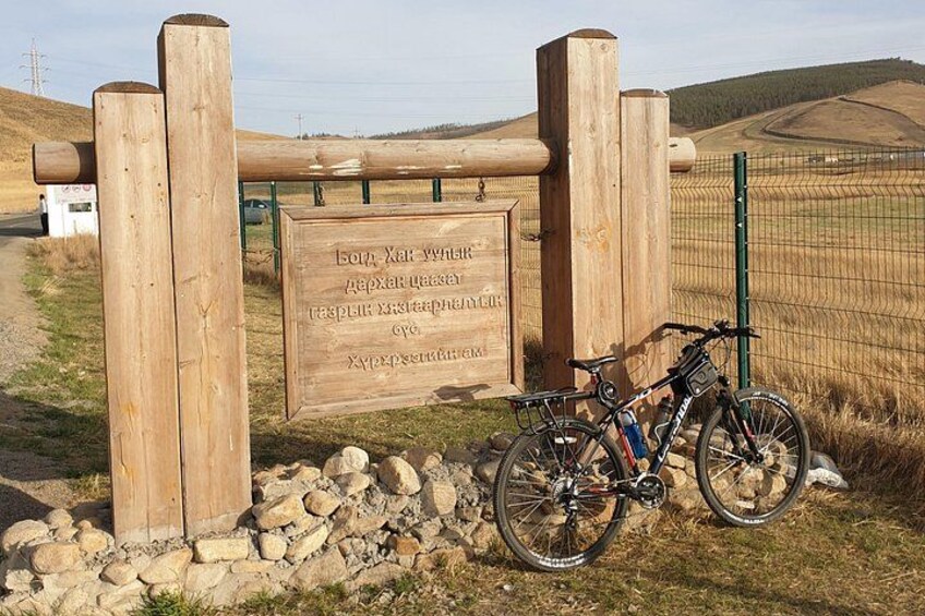 Un letrero de madera con texto, una bicicleta y un muro de piedra. 1