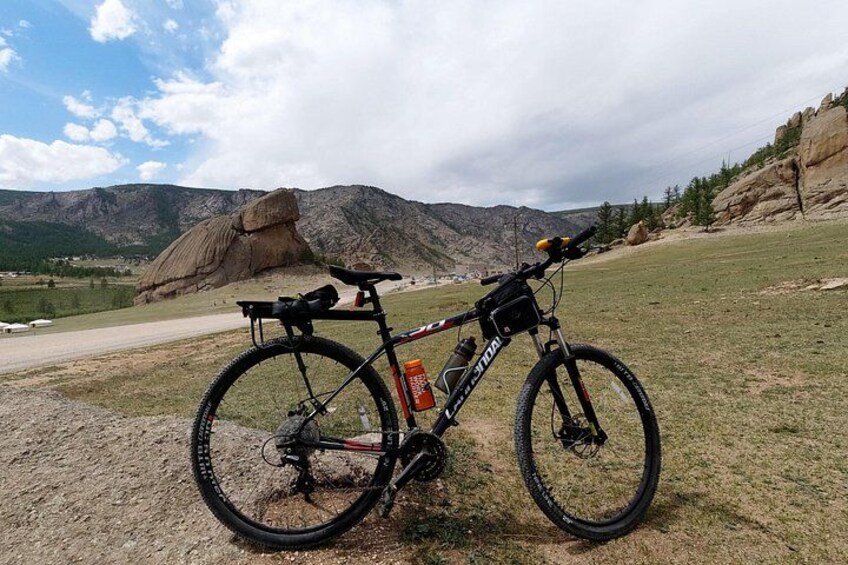 Una bicicleta de montaña estacionada en un campo cubierto de hierba, con una montaña rocosa al fondo. 3