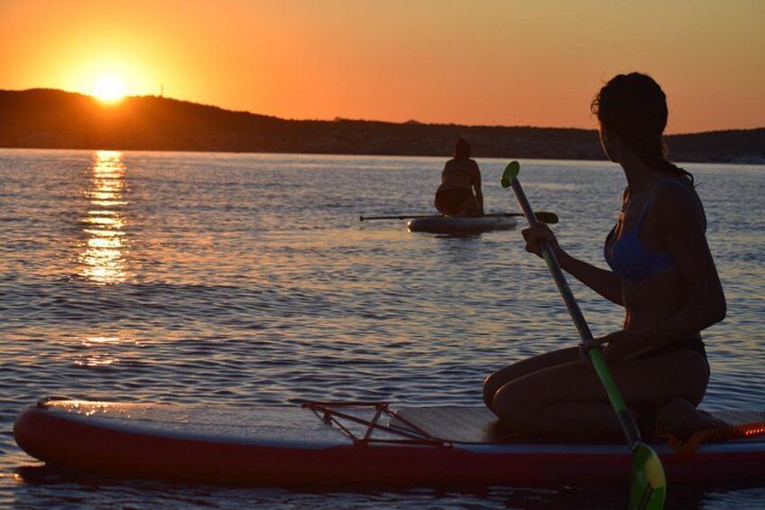 To personer står på paddleboards på et roligt vandstykke i solnedgangen. 2