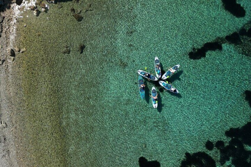 Ovenudblik over en strand med klart turkis vand og en gruppe paddleboards arrangeret i en cirkel. 3