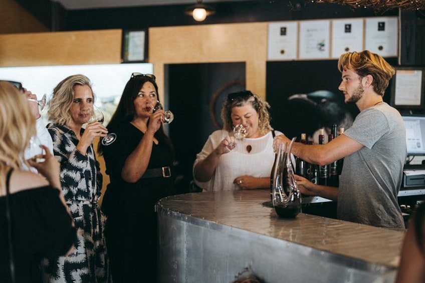 A bar setting with people standing around a bar counter, a bartender serving drinks, and a menu board in the background. 5
