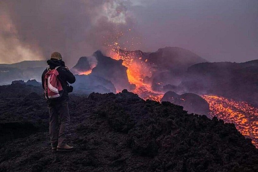 Una persona observando una erupción volcánica con lava fluyendo. 3