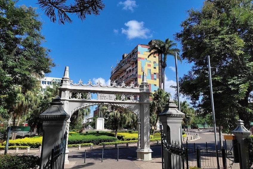 Un arco decorativo con diseños intrincados, rodeado de abundante follaje y un cielo azul despejado. 3