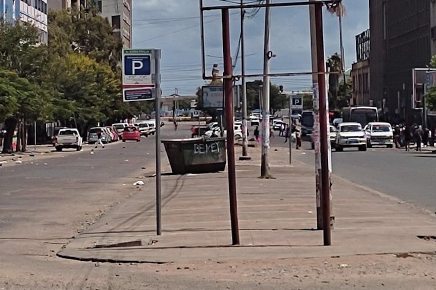 Una calle con una señal de estacionamiento, un contenedor verde y edificios al fondo. 5