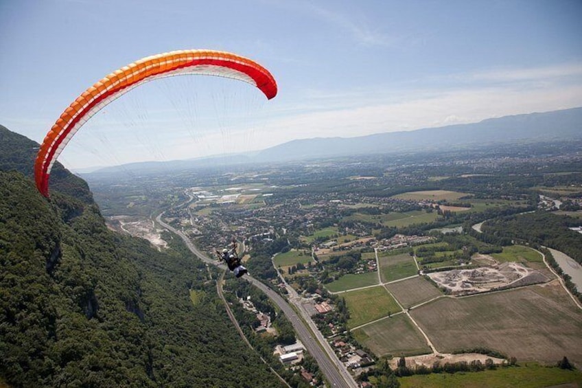 Un parapente descend vers une vallée où l’on aperçoit une rivière, des champs et, au loin, une chaîne de montagnes. 4