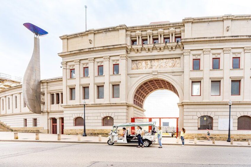 A historic building with an arched entrance, a unique sculpture, and a street with pedestrians and a vintage car. 5