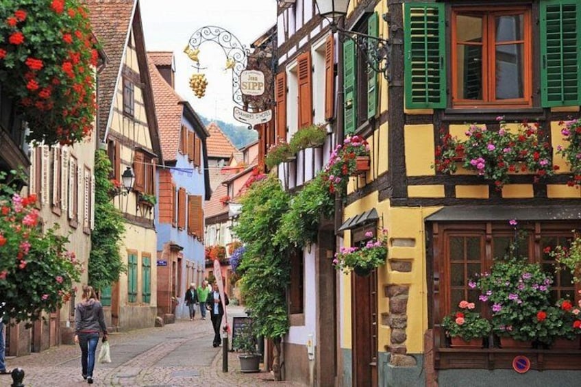 Eine enge Kopfsteinpflasterstraße gesäumt von bunten Fachwerkhäusern, von denen einige mit Blumenkästen und Ampeln geschmückt sind. 4