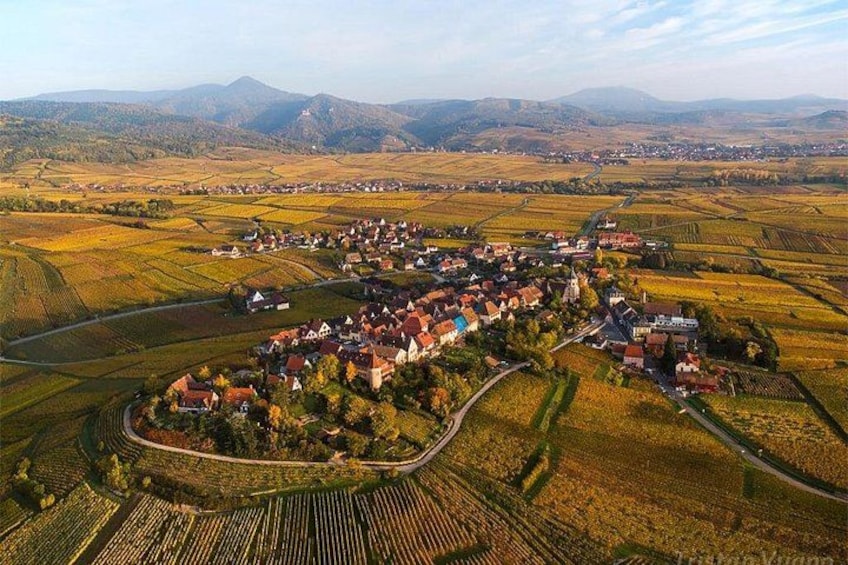 Ein ländliches Dorf mit Häusern, Feldern und sanften Hügeln im Hintergrund. 2
