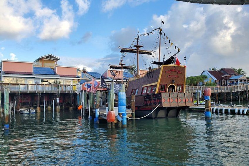 A large ship docked at a pier with a colorful design, surrounded by waterfront buildings and a clear sky. 1