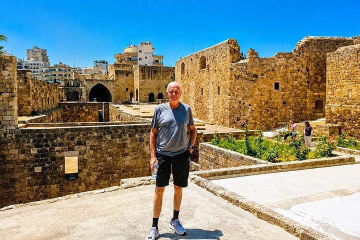 A man standing in front of ancient stone walls with a cityscape in the background. 4