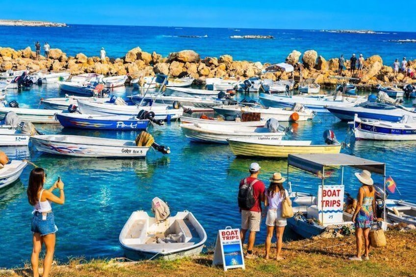 A marina with numerous boats docked, a sign for boat trips, and people near the water. 2