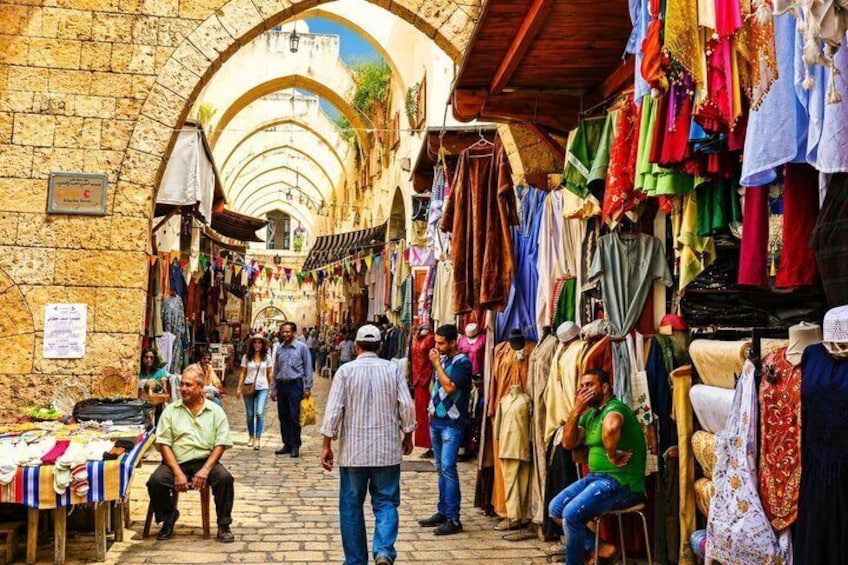 A bustling market with stone arches, colorful textiles, and people shopping. 5