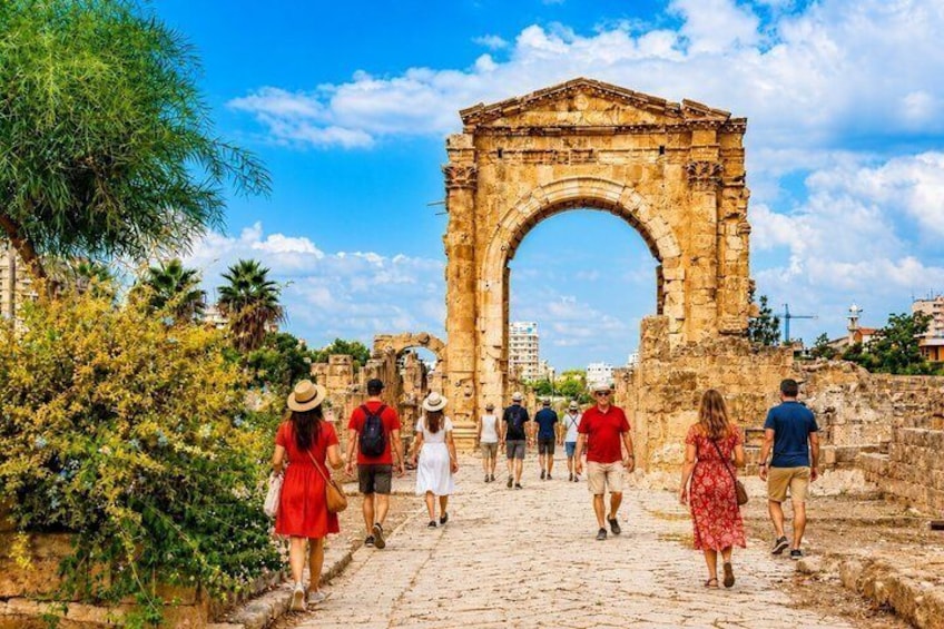 En historisk triumfbåge med turister som promenerar mot den. 1