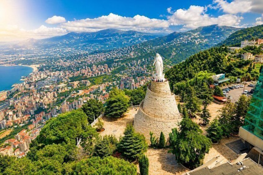 Un paisaje urbano costero con un monumento de piedra destacado en una colina, rodeado de vegetación y edificios. 5