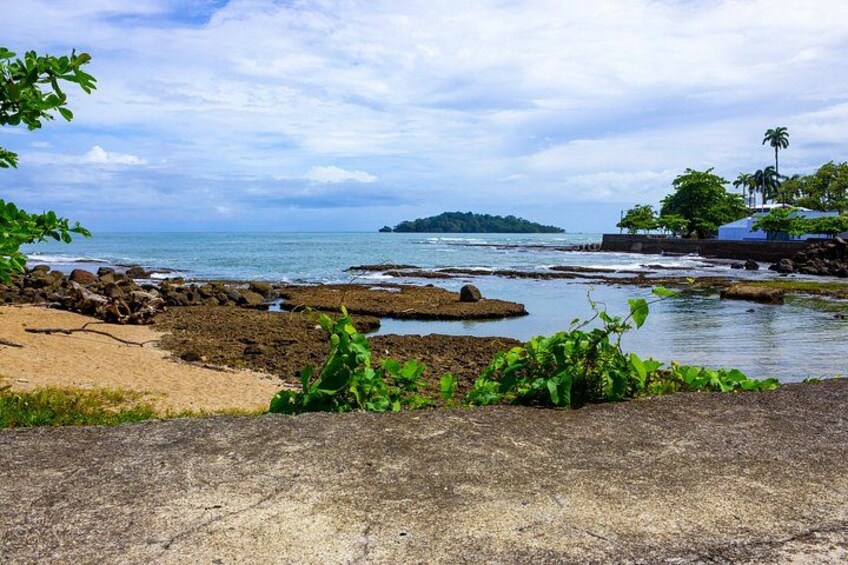 A coastal landscape with rocky shores, a sandy beach, and a distant island. 2