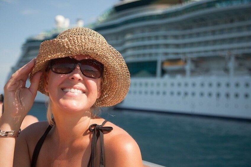 A person wearing a straw hat and a black swimsuit, with a cruise ship in the background. 1
