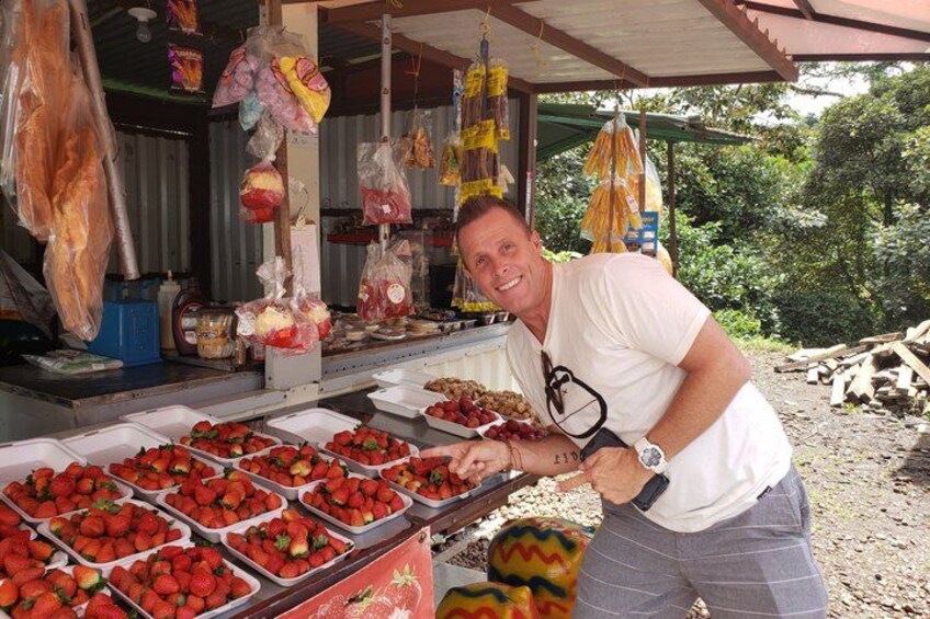 A person at a market stall with trays of strawberries and hanging meat products. 3