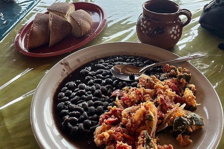 A plate of beans and meat, a cup, and bread on a table. 4