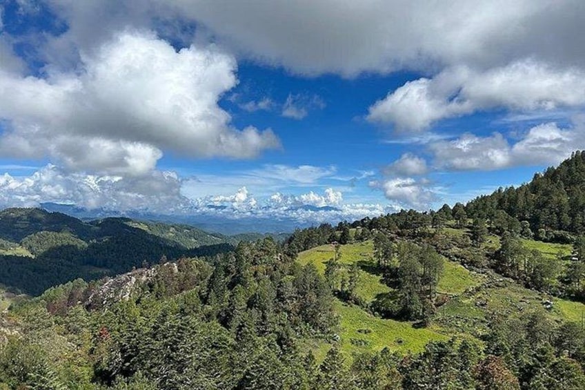 A mountainous landscape with dense forests, rolling hills, and a partly cloudy sky. 5