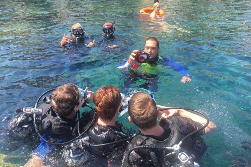 People in clear water, some wearing scuba gear, and one person taking a photo. 5