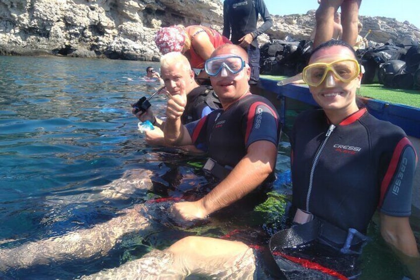 People in wetsuits and diving gear in shallow water, with rocky cliffs in the background. 4