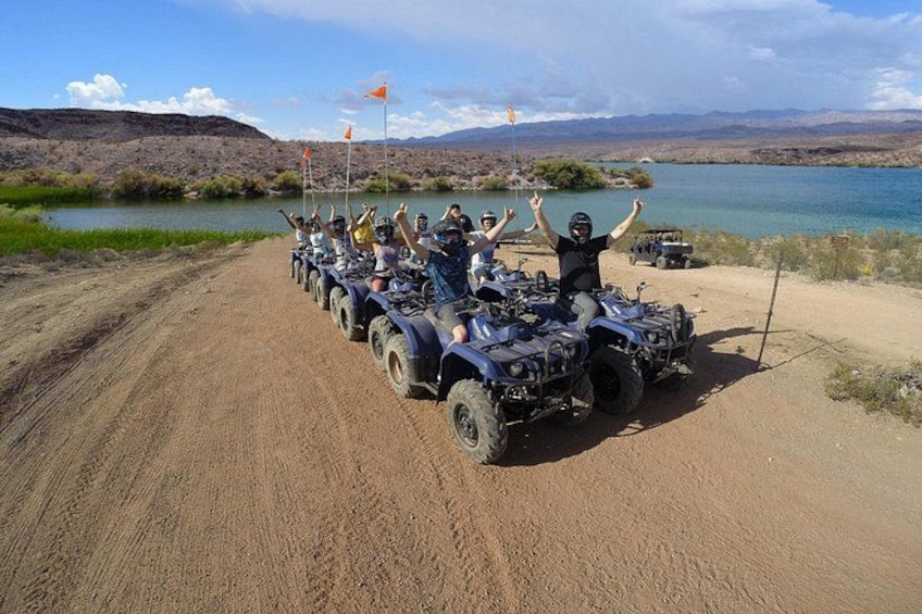 A group of people on ATVs on a dirt road by a lake. 3