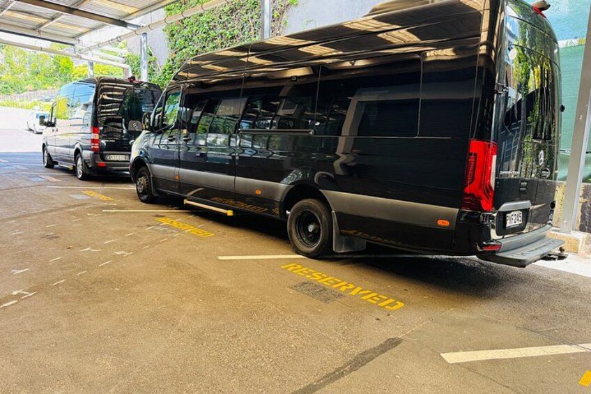A black van parked in a covered parking area with a yellow 'PARKED' marking on the ground. 2