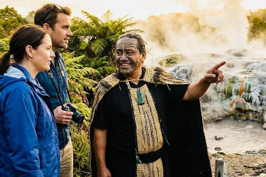 A person in traditional attire pointing, with a camera and a water feature in the background. 3