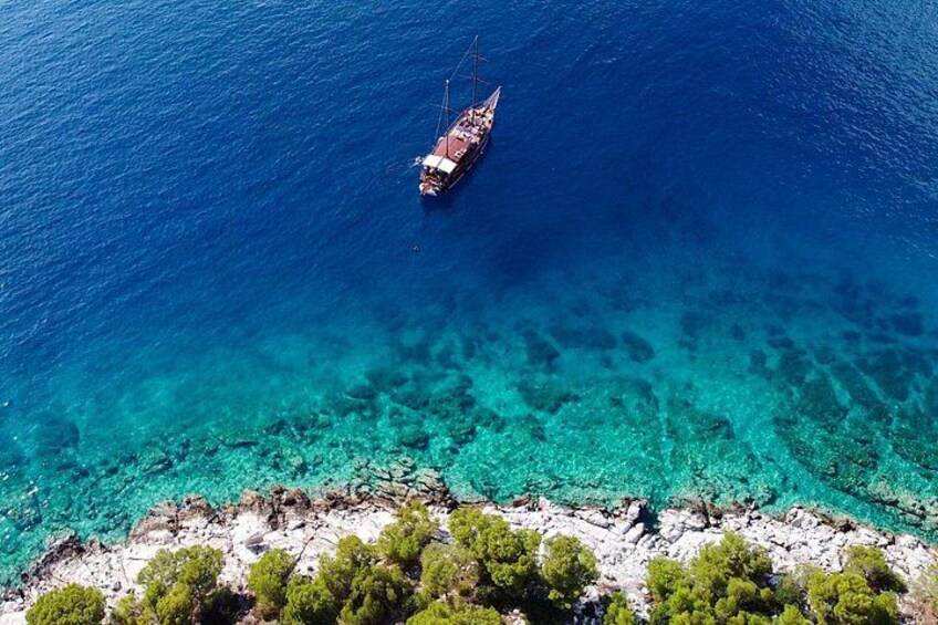 A ship anchored in clear blue waters with a rocky shoreline and green vegetation in the foreground. 1