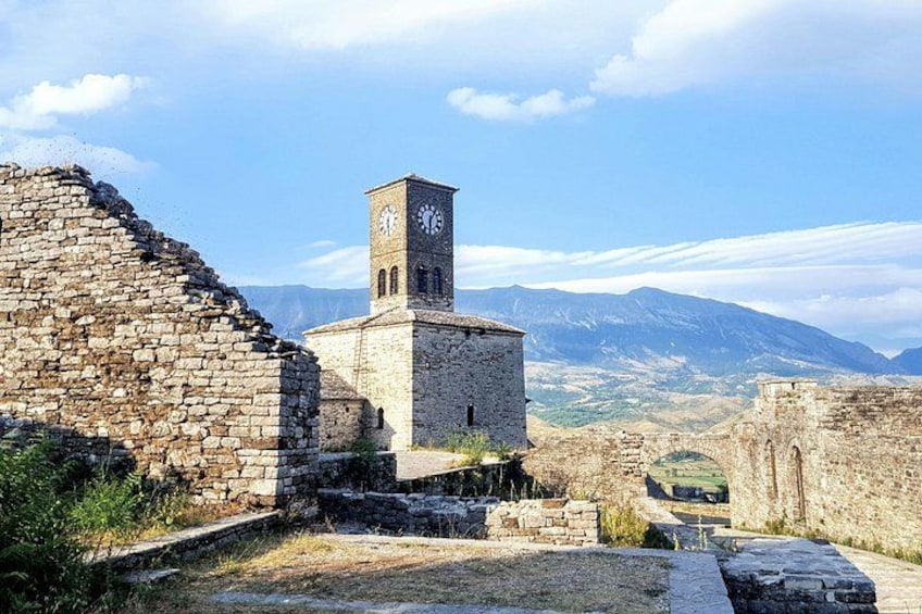 An ancient stone structure with a clock tower, surrounded by mountains and ruins. 2
