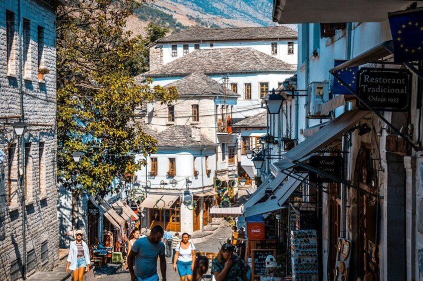 A narrow street in a European town with traditional buildings, a restaurant sign, and people walking. 3