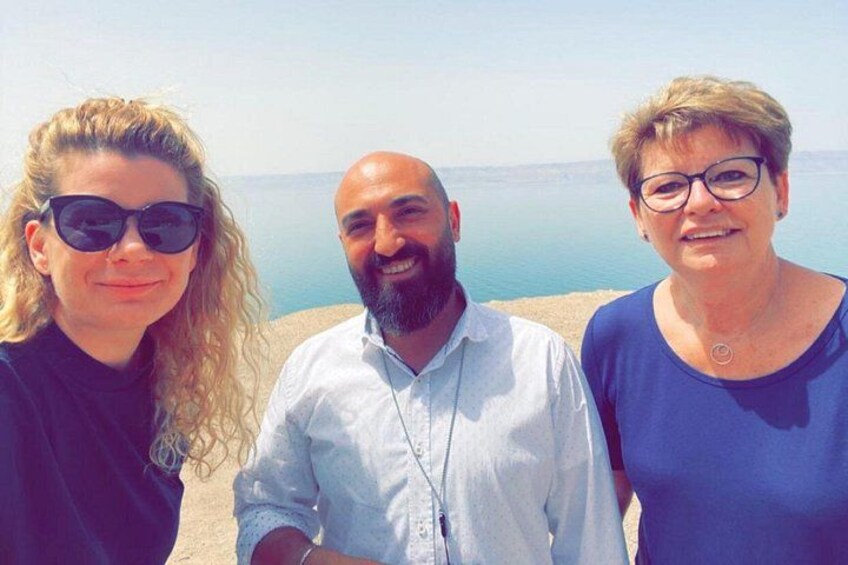Three people standing on a beach with a calm sea and clear sky in the background. 3