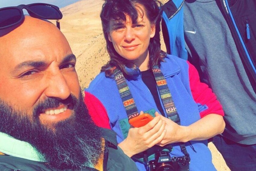 A person holding a camera, another person with a backpack, and a desert landscape in the background. 2