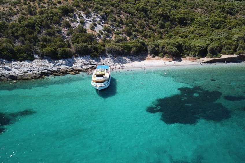 Un barco fondeado cerca de una costa rocosa con aguas turquesas cristalinas y una colina boscosa al fondo. 2