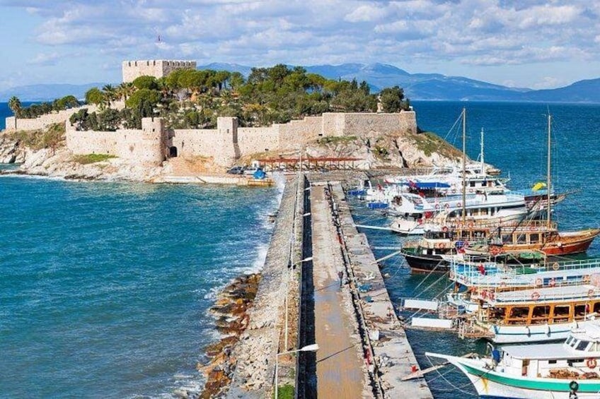 Un pueblo costero con un castillo fortificado, un muelle con barcos y un mar azul cristalino. 1