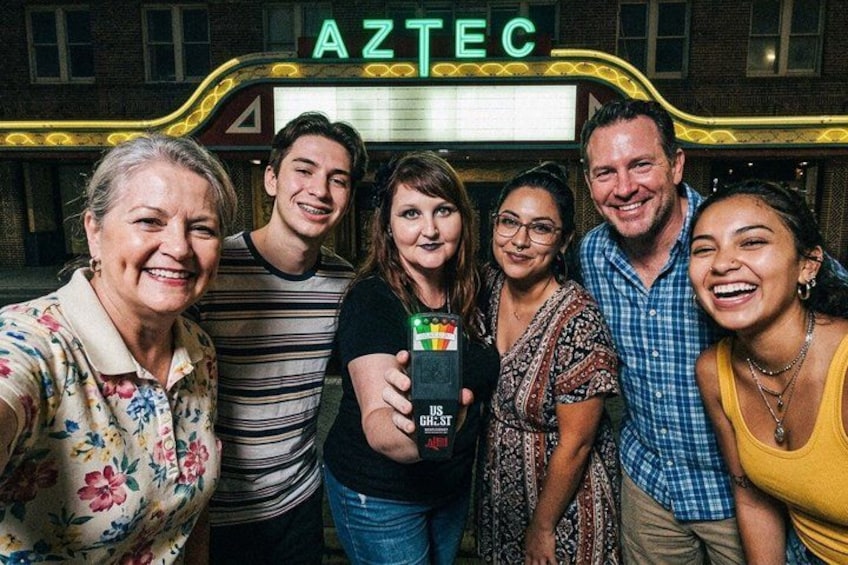 A group of people in front of a building with a sign that reads 'AZTEC.' 1