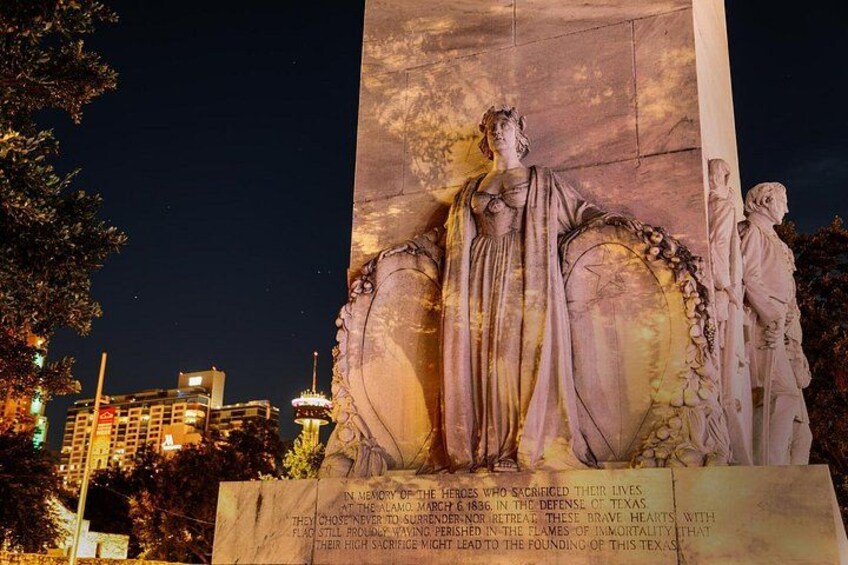 A monument with a statue of a woman and two children, illuminated at night. 2