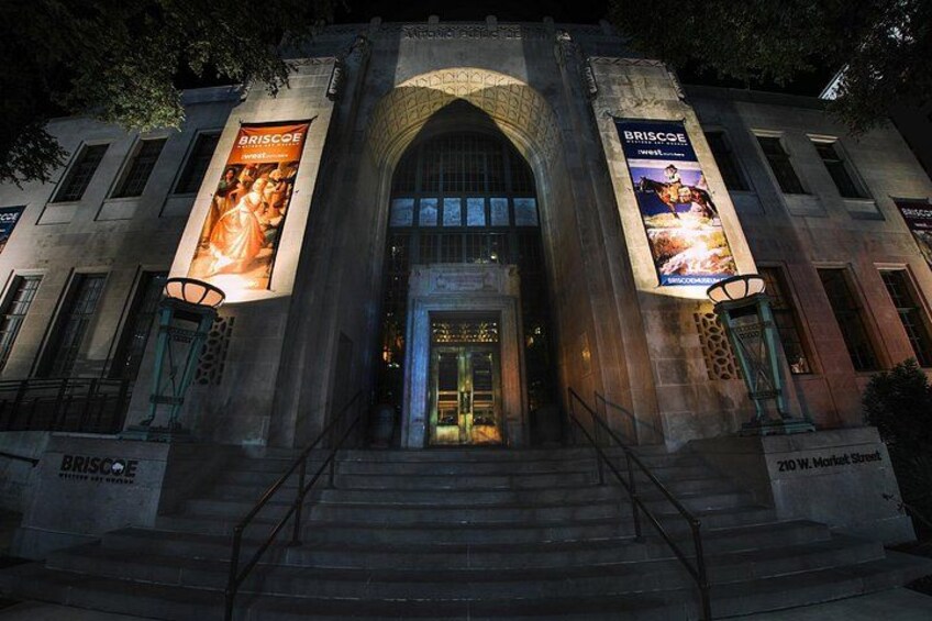 A historic building with a grand entrance, two large banners, and a staircase leading up to the door. 5